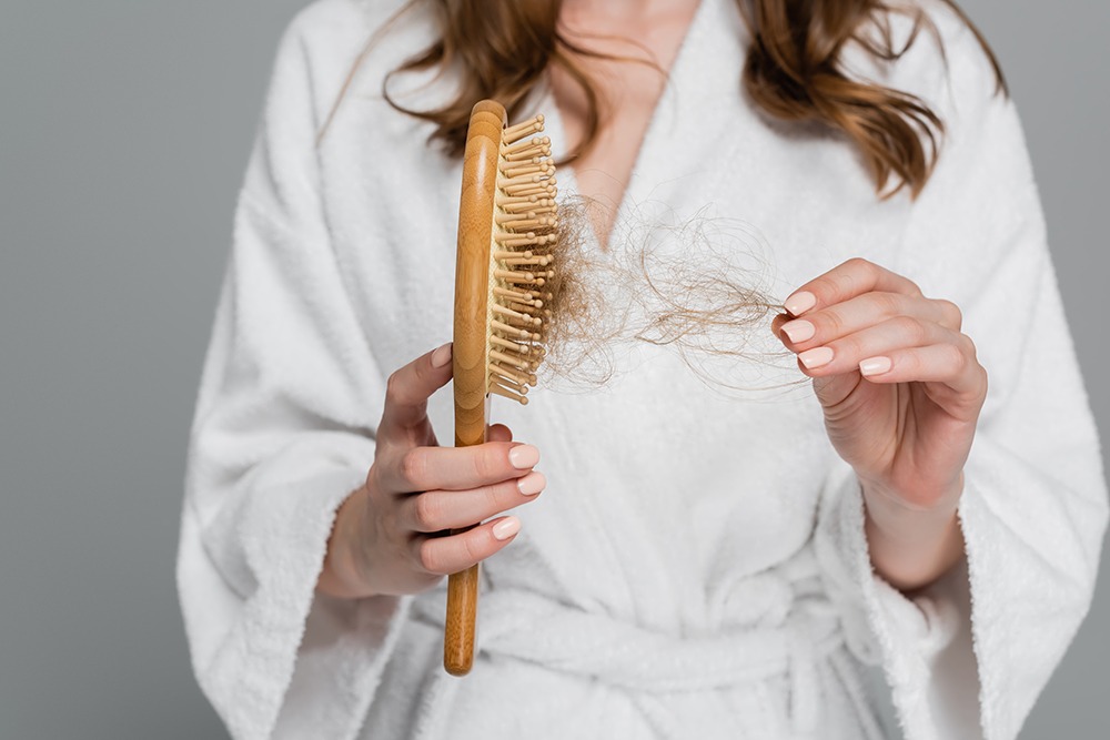 Serenity Emporium Hair Salon Cheadle - Home cropped view of young woman holding wooden hair brush and pulling damaged hair isolated on grey